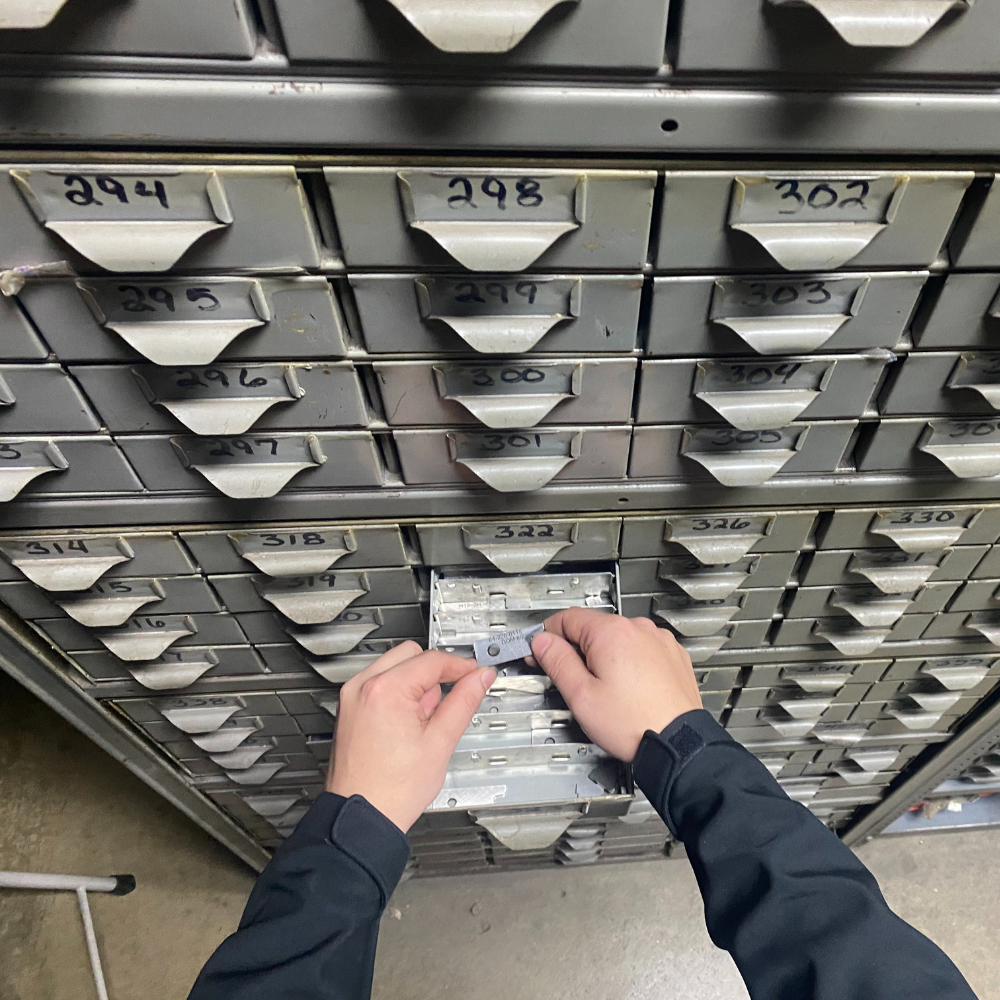 A worker's hand is holding metal ring object, a machinery spare part with blurred background of storage shelf. Industrial working scene photo, selective focus.